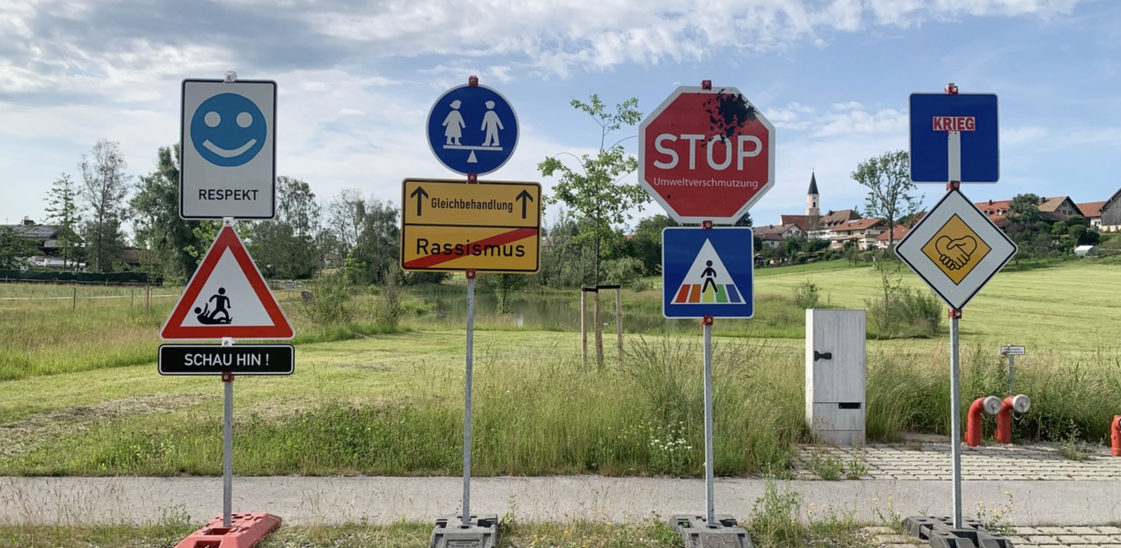 Verkehrsschilder mit Botschaften zu Respekt, Gleichbehandlung, Umweltschutz und Frieden auf einer Wiese.